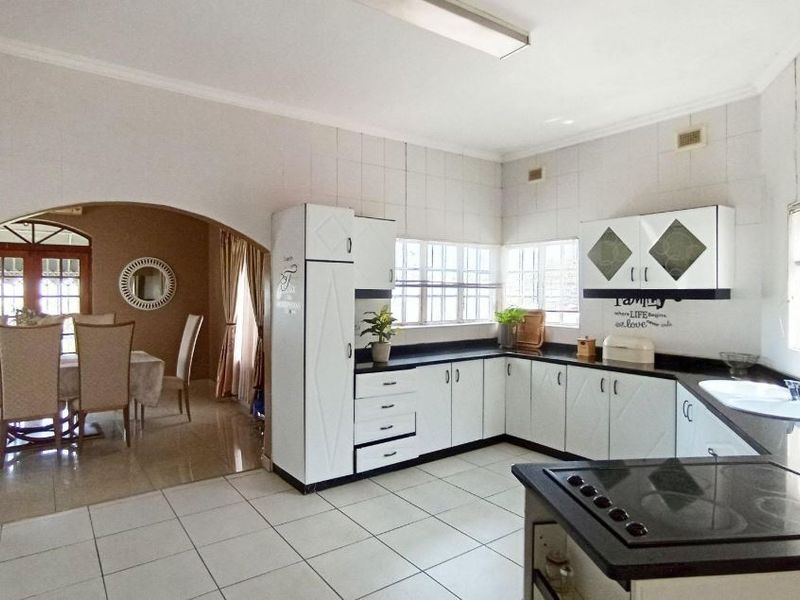 A functional kitchen featuring white cabinetry, dark countertops, and an electric hob, with an open-plan layout leading into the adjacent dining area.