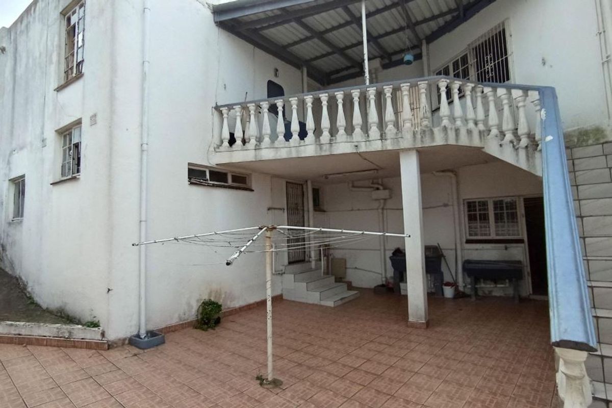 Rear exterior view featuring a covered patio area, tiled flooring, and an external staircase leading to an upper balcony with a balustrade.