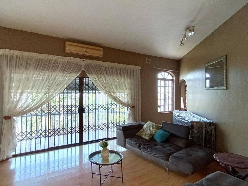 Spacious living room featuring laminate flooring, a vaulted ceiling, and large sliding glass doors with security gates leading to an outdoor area.
