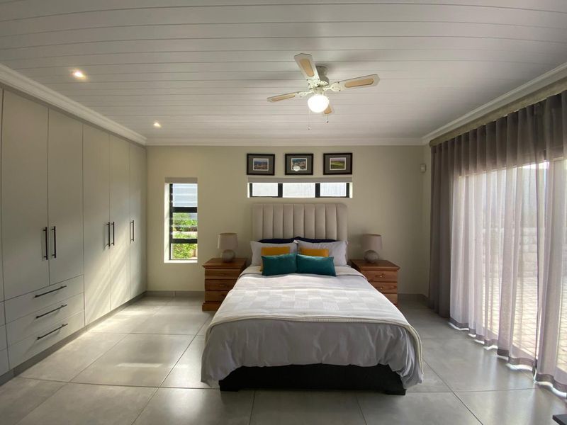 A well-maintained bedroom featuring neutral tiled floors, extensive built-in cabinetry, a ceiling fan, and large sliding doors providing natural light.
