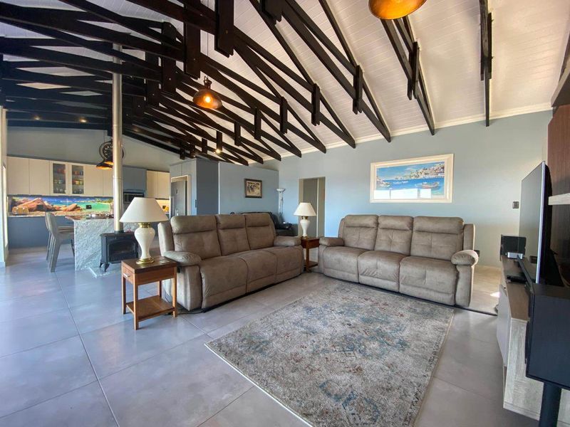Spacious open-plan living area featuring high vaulted ceilings with exposed timber rafters, a wood-burning fireplace, and a modern kitchen with stone island.