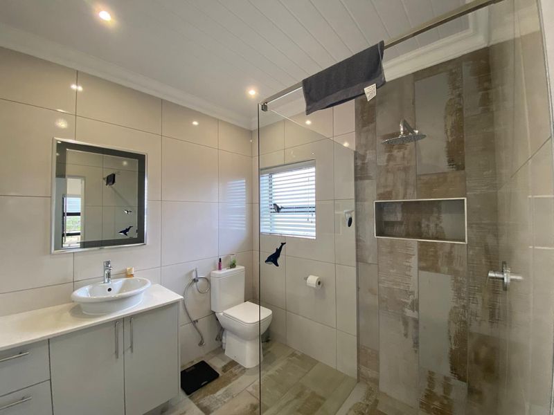 Modern bathroom featuring a glass-enclosed shower with a rain shower head, a vessel sink vanity, and neutral wall and floor tiling.