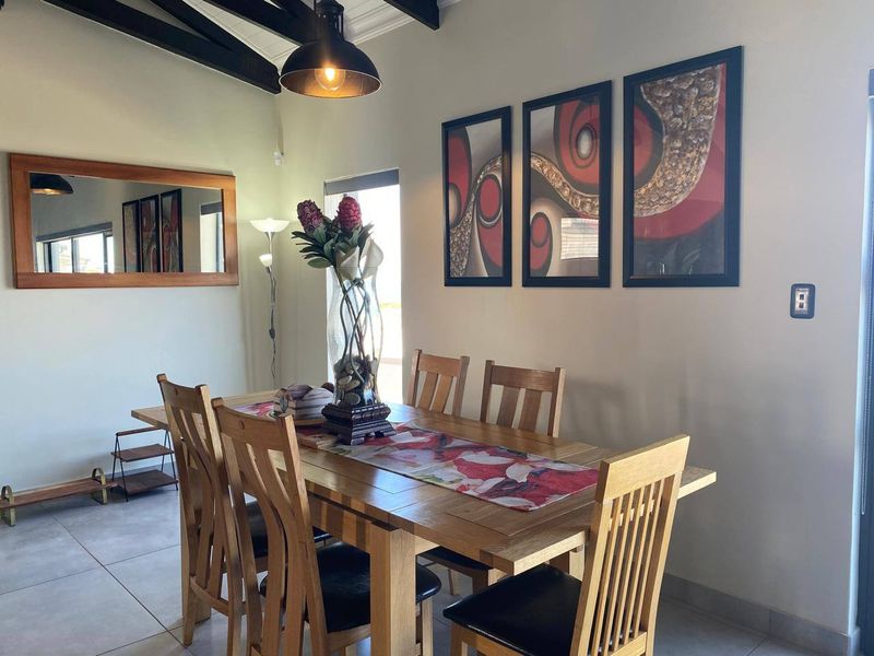 A well-lit dining room featuring exposed timber ceiling beams, tiled flooring, and a modern pendant light fixture.