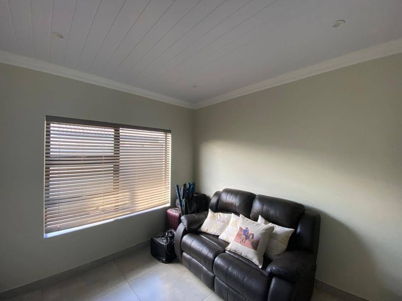 A living room featuring tiled flooring, a tongue and groove ceiling with recessed lighting, and fitted venetian blinds.