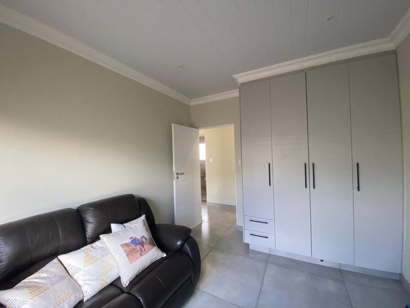 A well-maintained bedroom featuring neutral walls, large-format floor tiles, recessed ceiling lighting, and ample built-in cupboard storage.