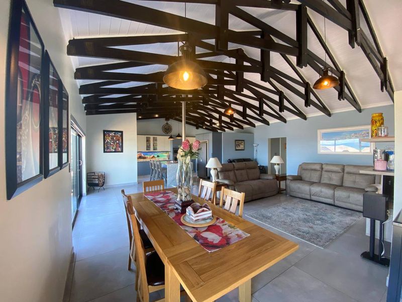 Spacious open-plan living and dining area featuring high vaulted ceilings with exposed timber trusses, tiled flooring, and seamless access to outdoor spaces.