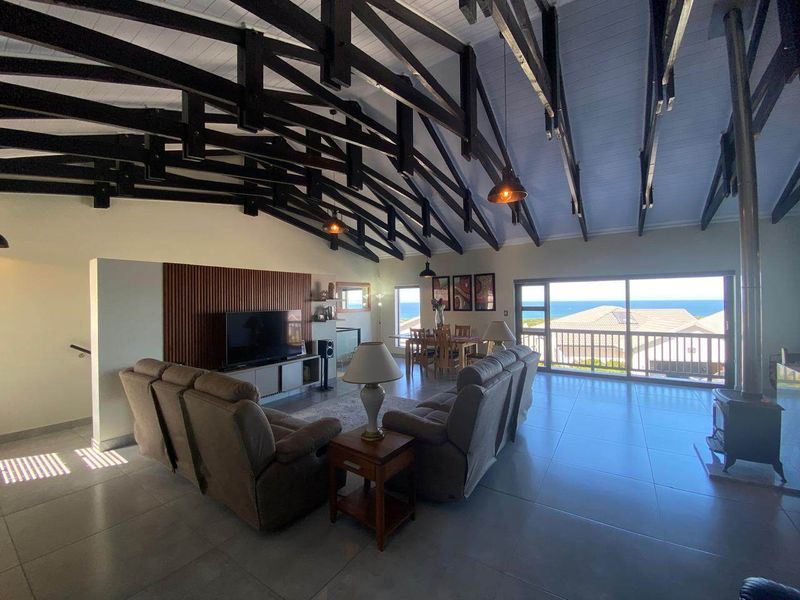 Spacious open-plan living and dining area featuring high vaulted ceilings with exposed timber trusses, large sliding doors, and a modern freestanding fireplace.