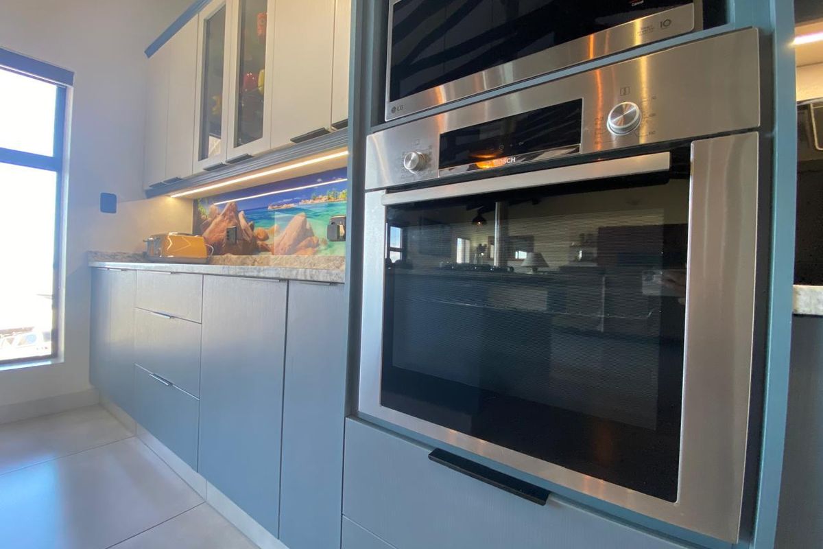 Modern kitchen featuring sleek blue cabinetry, integrated stainless steel oven and microwave, stone countertops, and under-cabinet lighting.