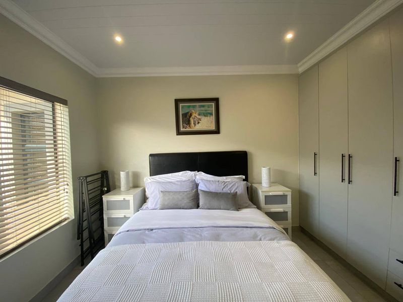 A well-maintained bedroom featuring neutral walls, built-in cupboards, recessed downlighting, and tiled flooring with venetian blinds.