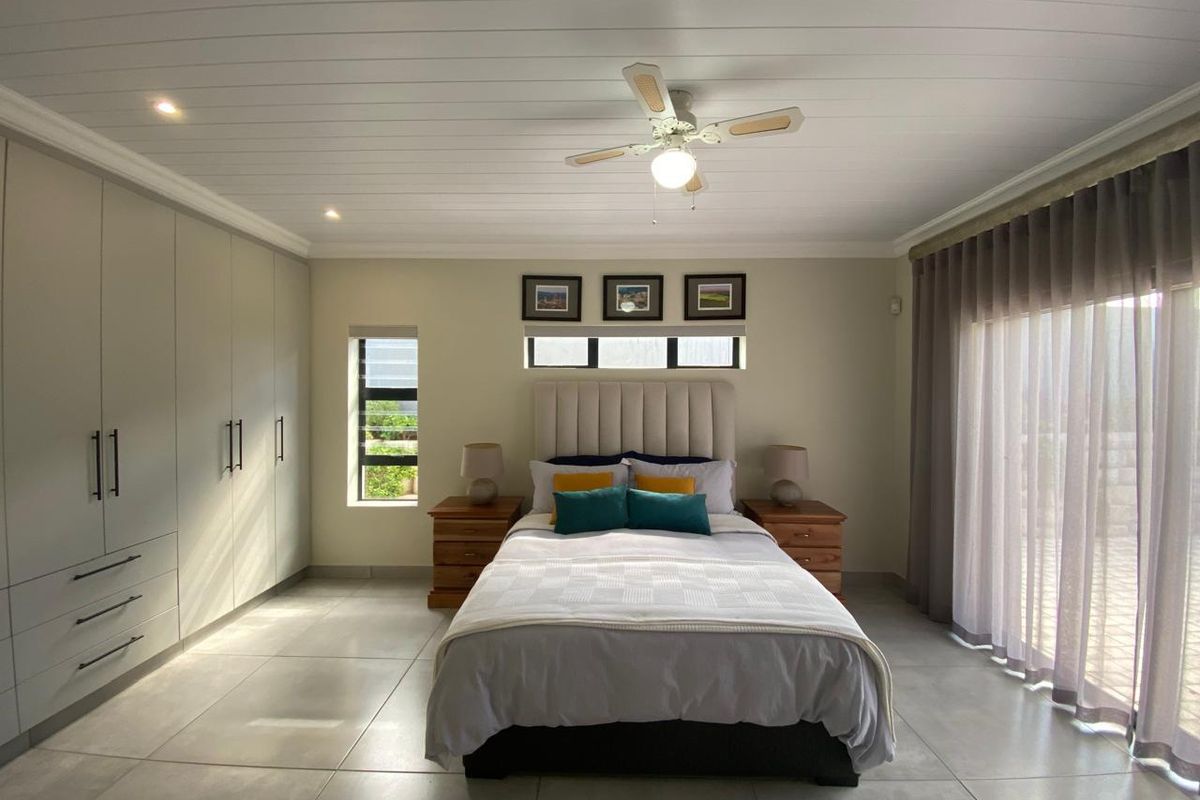 A well-maintained bedroom featuring neutral tiled floors, extensive built-in cabinetry, a ceiling fan, and large sliding doors providing natural light.