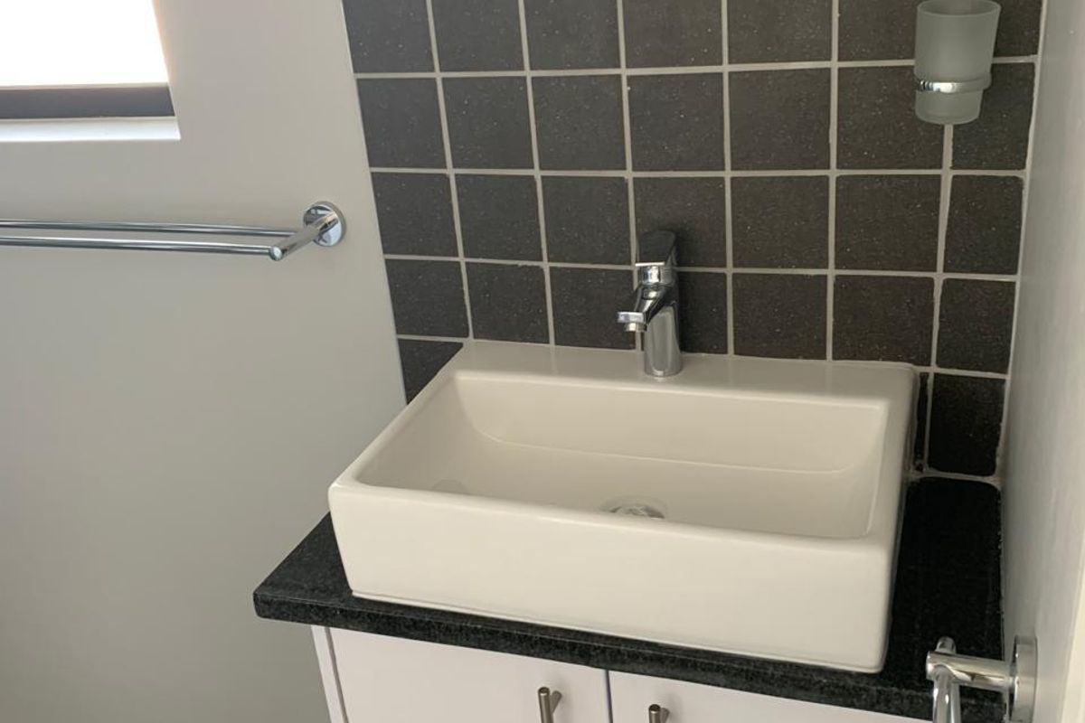 A clean and modern bathroom vanity featuring a white vessel sink, dark stone countertop, and a tiled splashback.