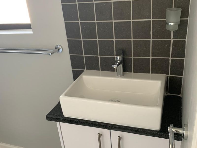 A clean and modern bathroom vanity featuring a white vessel sink, dark stone countertop, and a tiled splashback.