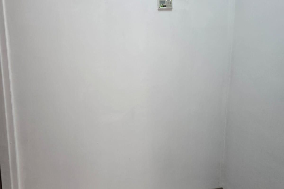 A clean, empty utility space featuring tiled flooring, a security alarm keypad, and a high-level glass block window for natural light.