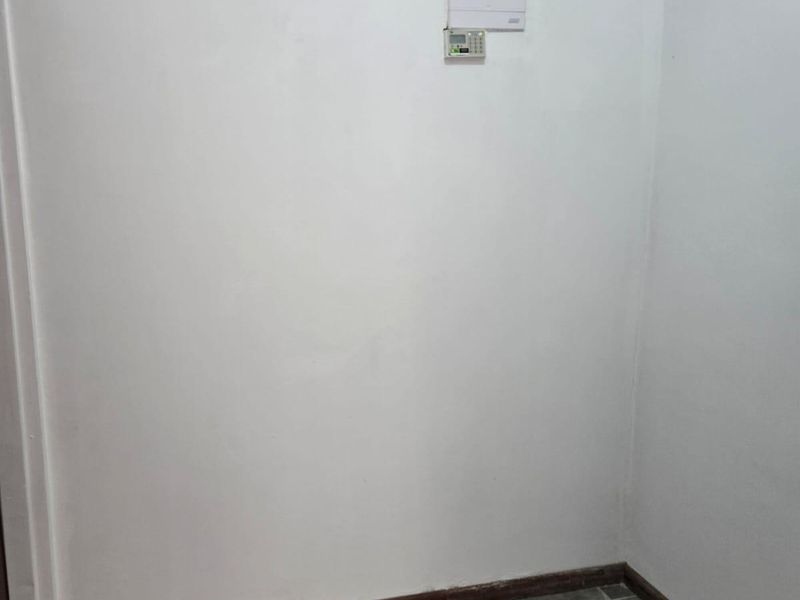 A clean, empty utility space featuring tiled flooring, a security alarm keypad, and a high-level glass block window for natural light.