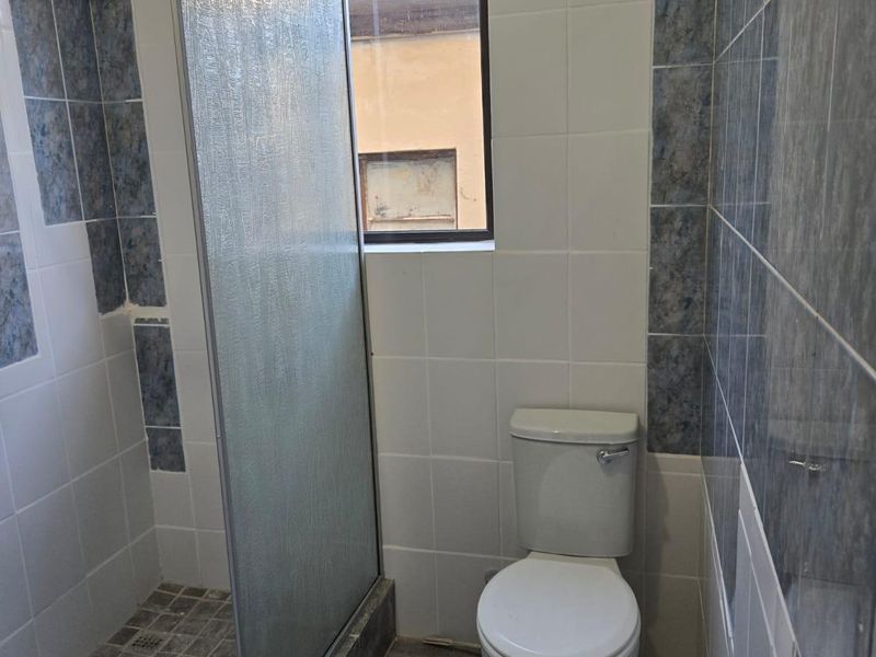 A functional bathroom featuring a walk-in shower with a glass screen, a standard toilet, and neutral tiled finishes throughout.