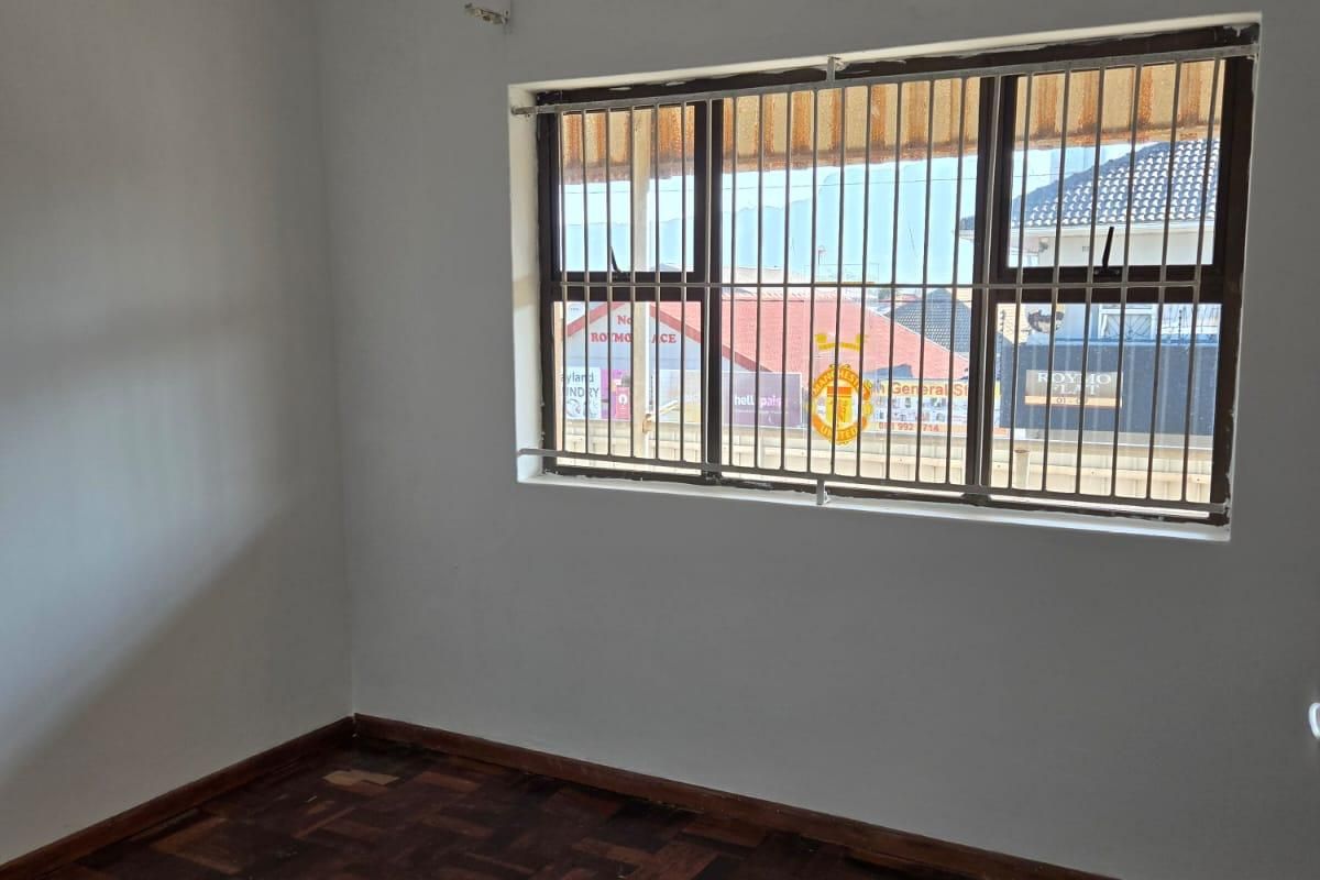 An empty bedroom featuring traditional parquet flooring and a window fitted with security bars.