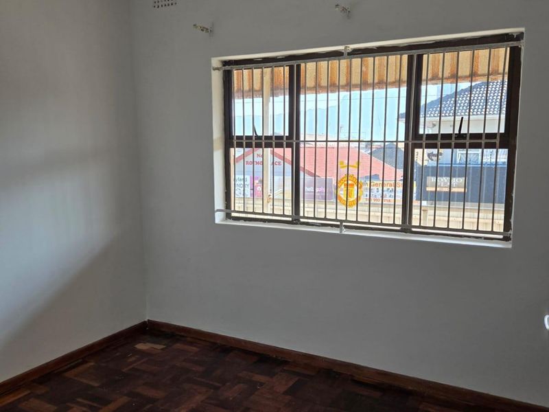 An empty bedroom featuring traditional parquet flooring and a window fitted with security bars.