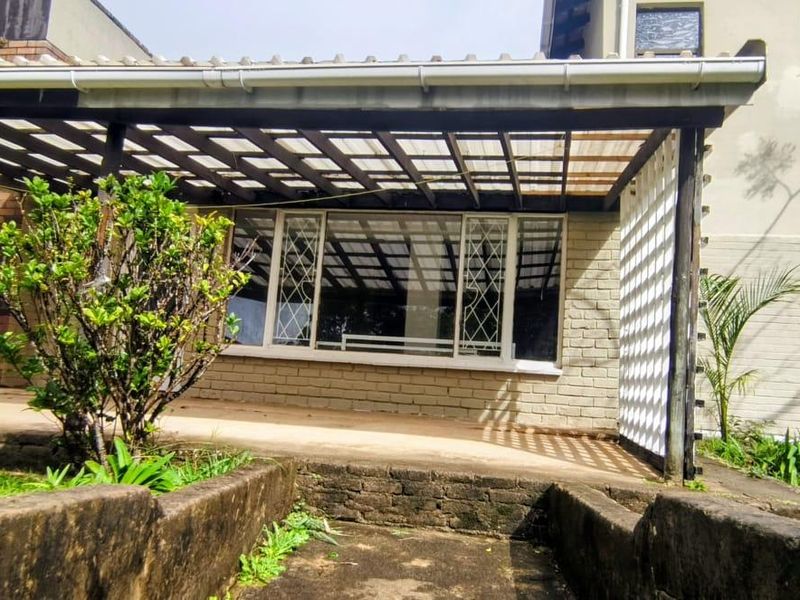 A covered outdoor patio area featuring a timber pergola structure, brick masonry walls, and security-barred windows, offering potential for an updated entertainment space.