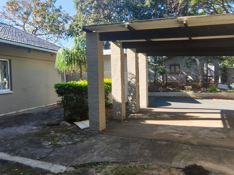 A functional exterior view featuring a covered carport, concrete driveway, and direct access to the main house entrance with security gate.