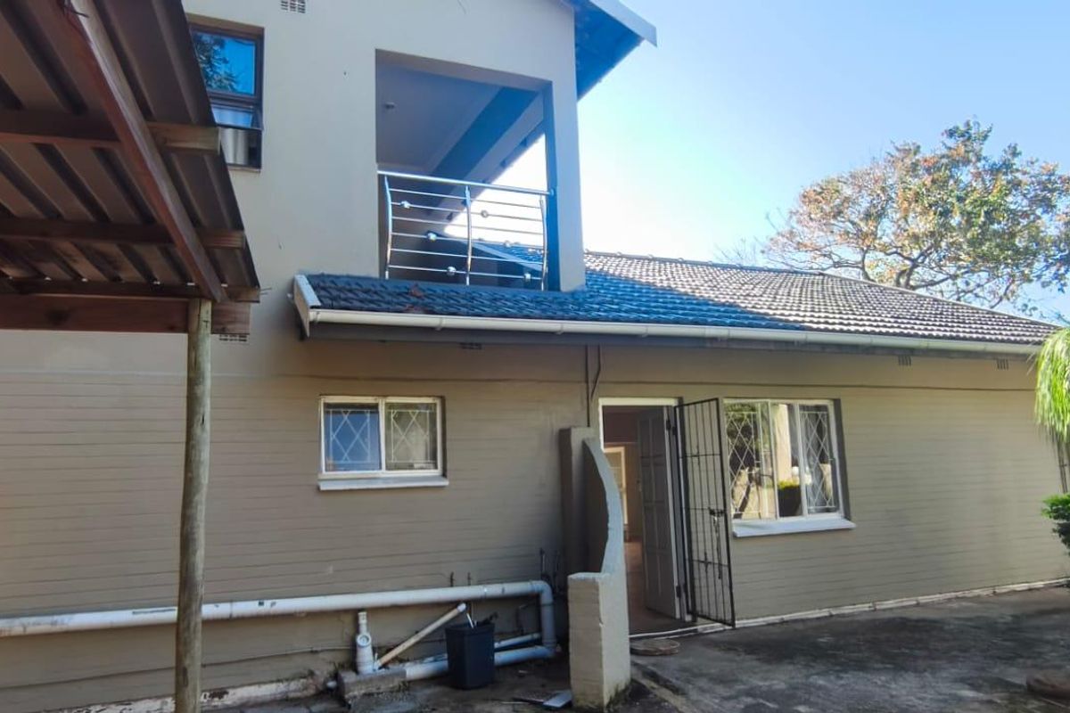 Rear view of the house featuring a balcony with stainless steel balustrade, security gates, and a concrete patio area with visible exterior plumbing.