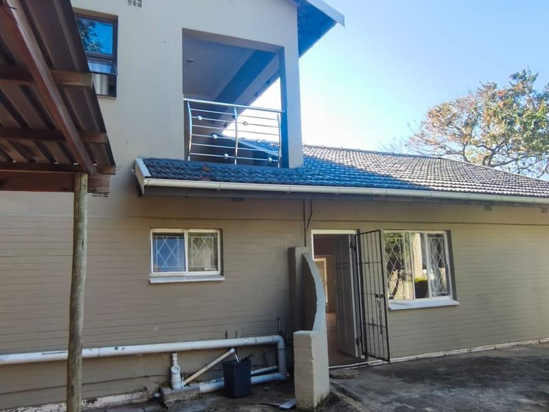 Rear view of the house featuring a balcony with stainless steel balustrade, security gates, and a concrete patio area with visible exterior plumbing.