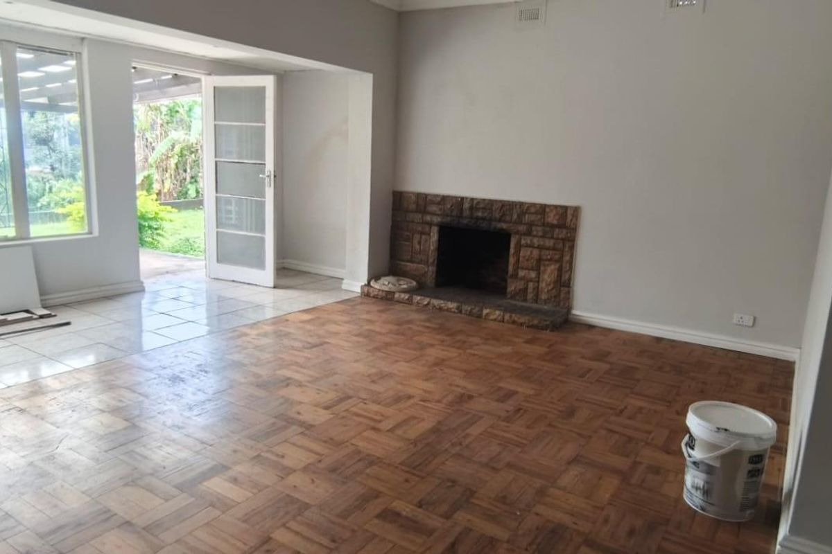 Spacious living room featuring original parquet flooring, a stone fireplace, and direct access to an outdoor patio area through glass doors.