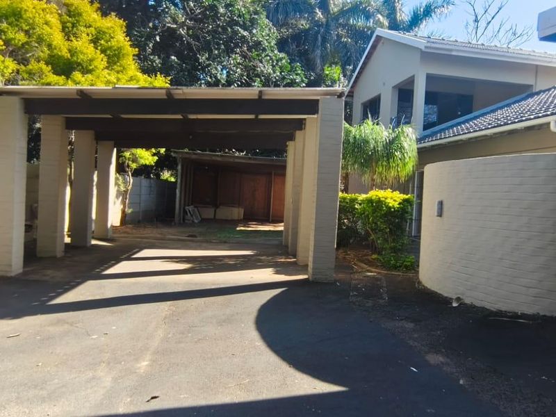 Exterior view of the property featuring a covered carport, asphalt driveway, and brick facade with a tiled roof.