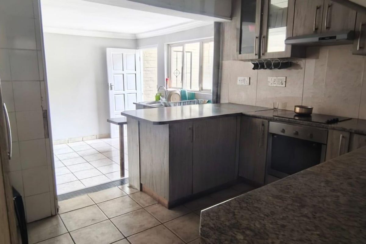 Functional kitchen featuring wood-look cabinetry, granite countertops, built-in oven and hob, and tiled flooring, with an adjacent utility or scullery area.