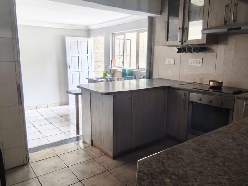 Functional kitchen featuring wood-look cabinetry, granite countertops, built-in oven and hob, and tiled flooring, with an adjacent utility or scullery area.