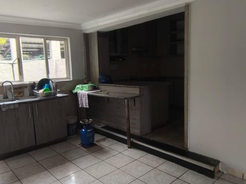 A functional scullery area featuring tiled flooring, a stainless steel sink, and built-in cabinetry, providing additional prep and wash-up space.