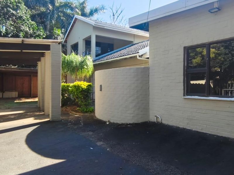 Exterior view of the property featuring a paved driveway, covered carport area, and brick facade with aluminum window frames.