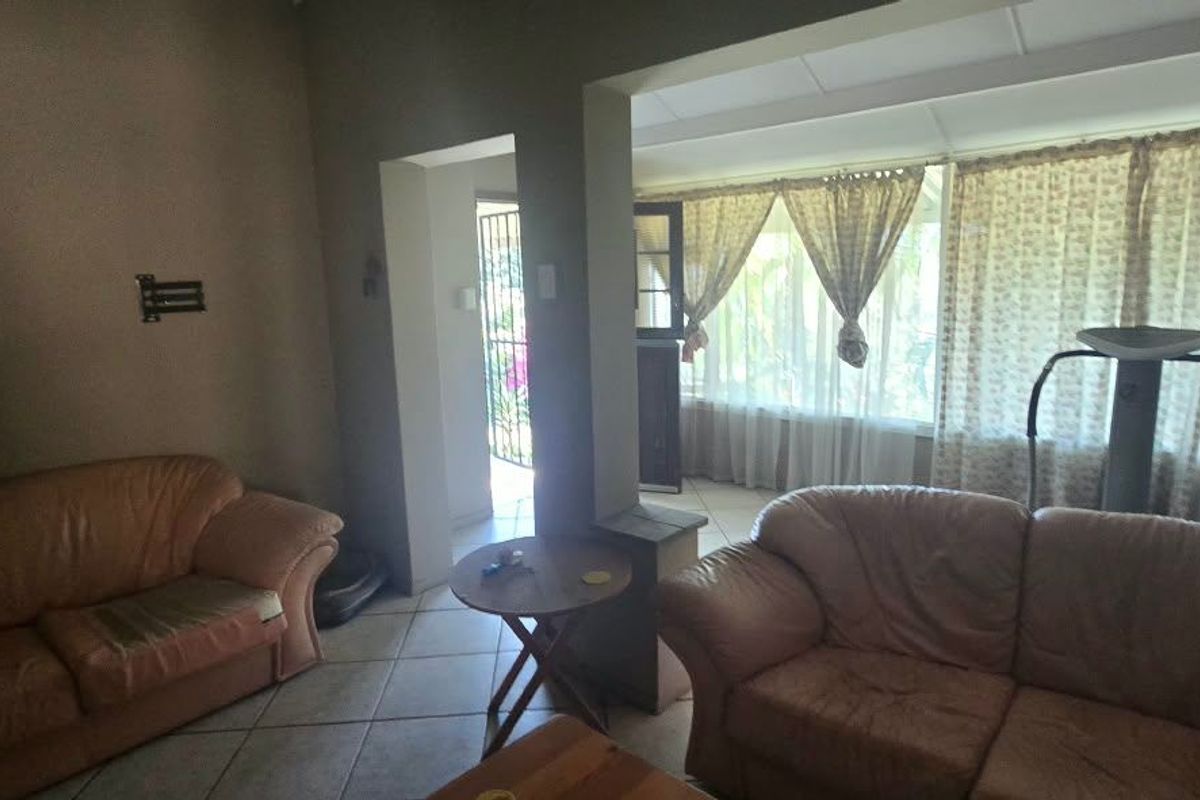 A living room area featuring tiled flooring and large windows, providing access to an adjacent sunroom or patio space through a doorway.