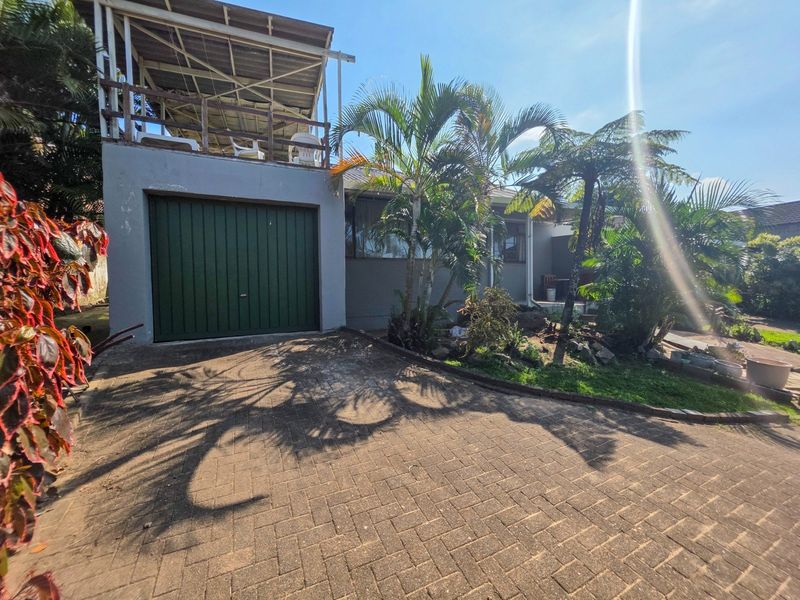 Front exterior view of the house featuring a paved driveway, a garage, and a raised balcony area with established garden landscaping.