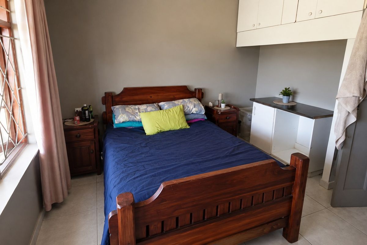A functional bedroom featuring tiled flooring, built-in storage cupboards, and security bars on the window.