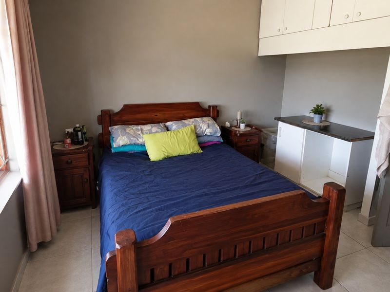 A functional bedroom featuring tiled flooring, built-in storage cupboards, and security bars on the window.