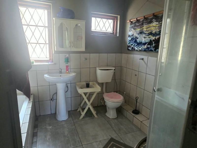 A functional bathroom featuring a pedestal basin, toilet, shower enclosure, and tiled finishes, offering a practical layout with natural light from leaded glass windows.
