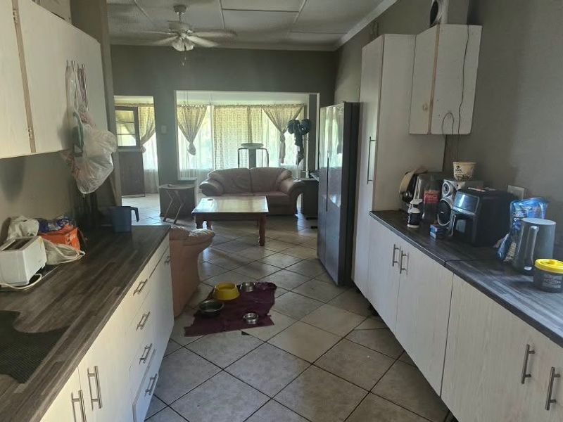 Open-plan kitchen and living area featuring tiled flooring, laminate cabinetry, and a ceiling fan, offering a functional layout with potential for modernization.