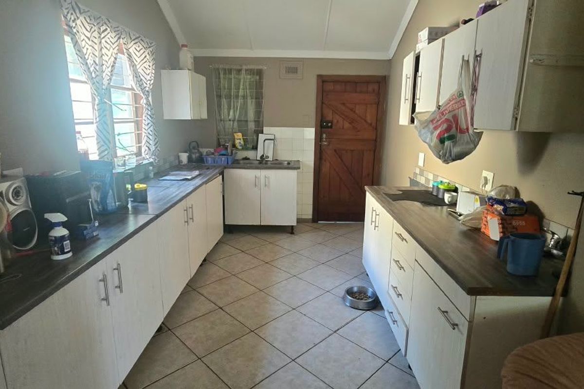A functional kitchen featuring laminate countertops, built-in cabinetry, and tiled flooring, offering a practical layout with direct access to an exterior door.