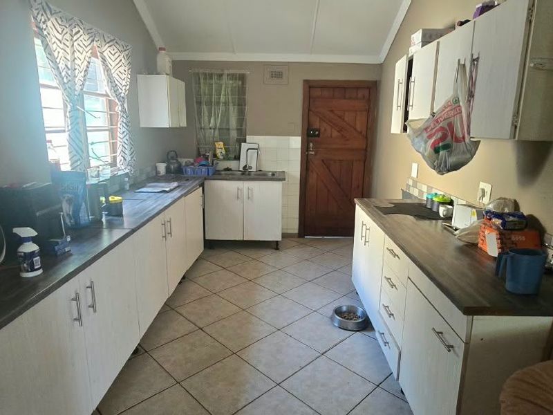 A functional kitchen featuring laminate countertops, built-in cabinetry, and tiled flooring, offering a practical layout with direct access to an exterior door.
