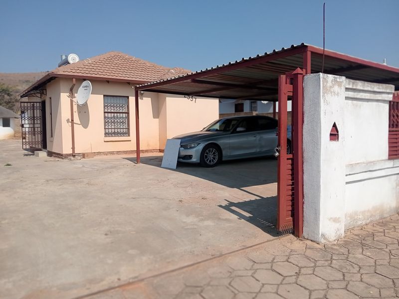 Front exterior view of the house featuring a covered carport, concrete driveway, and perimeter wall with a metal gate.