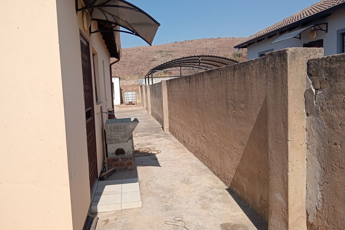 A narrow rear exterior walkway featuring a concrete boundary wall, a utility sink, and a protective door awning.