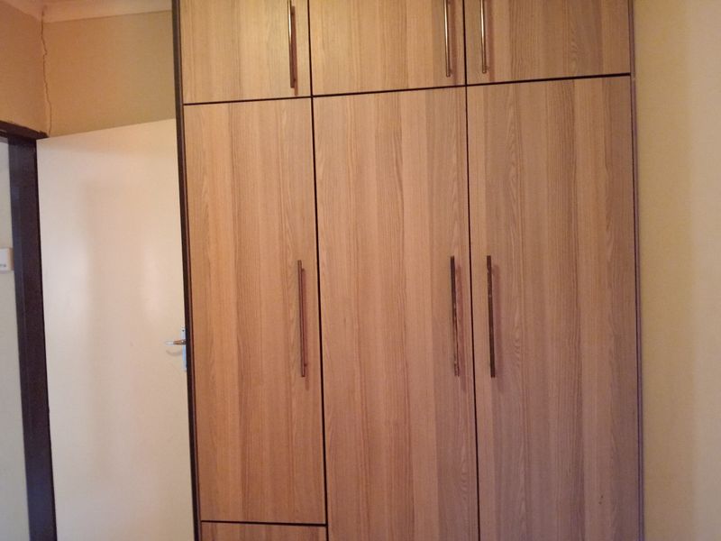 A bedroom featuring floor-to-ceiling built-in wooden cupboards with modern handles, showing minor wall cracking near the door frame.