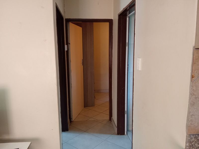 A functional hallway featuring tiled flooring and multiple doorways leading to adjacent rooms, showing signs of wear on the walls and door frames.