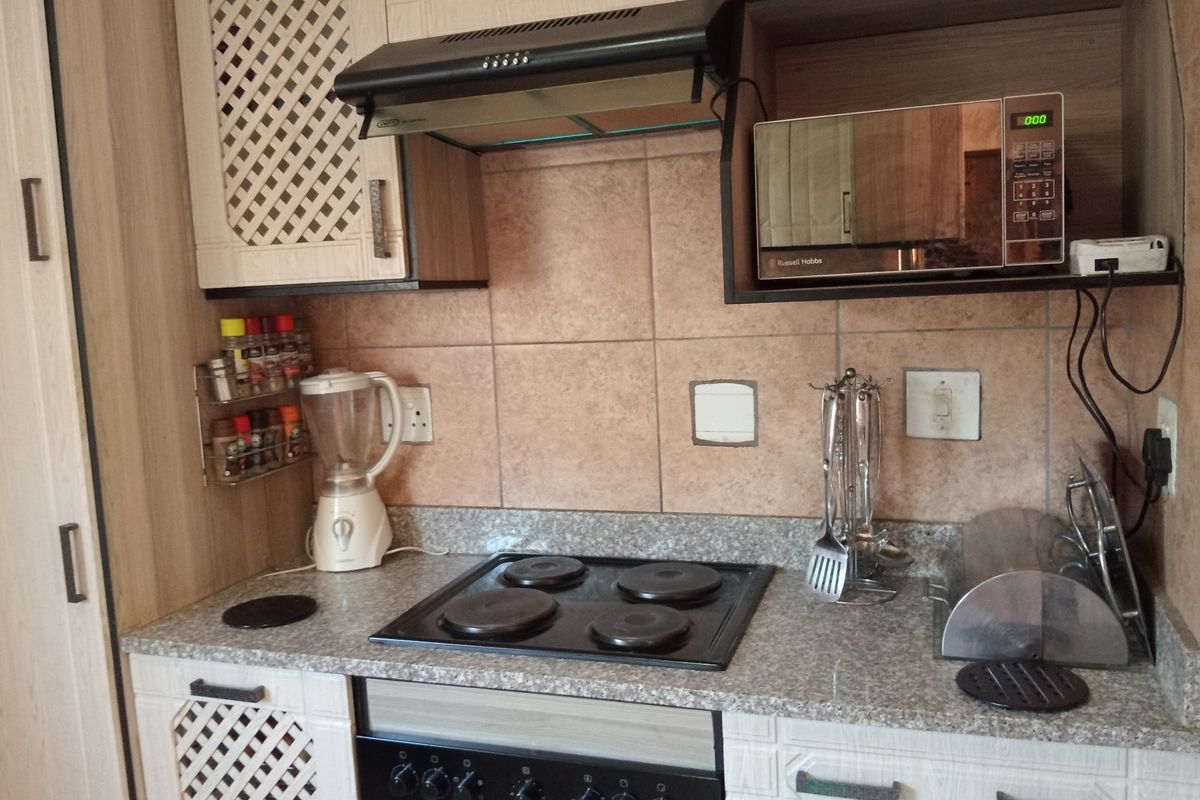 A functional kitchen featuring built-in cabinetry, a granite countertop, tiled backsplash, and integrated appliances including an electric hob, oven, and extractor fan.