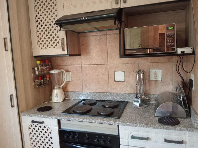 A functional kitchen featuring built-in cabinetry, a granite countertop, tiled backsplash, and integrated appliances including an electric hob, oven, and extractor fan.