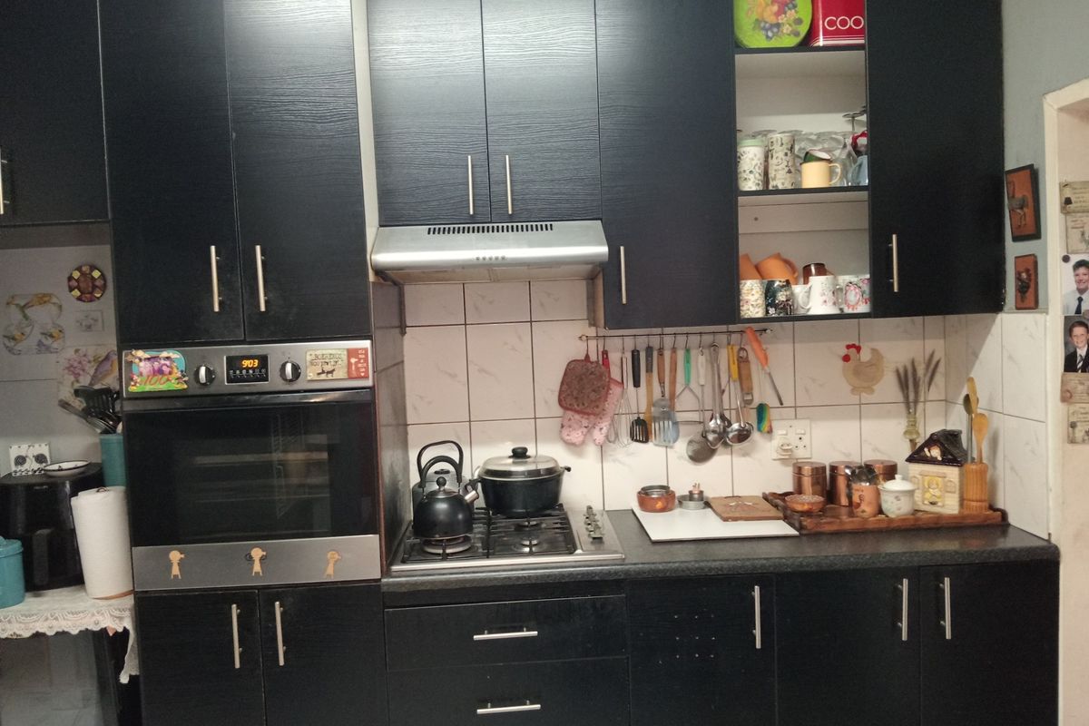 A functional kitchen featuring dark laminate cabinetry, a built-in oven, gas hob, extractor fan, and a tiled backsplash.