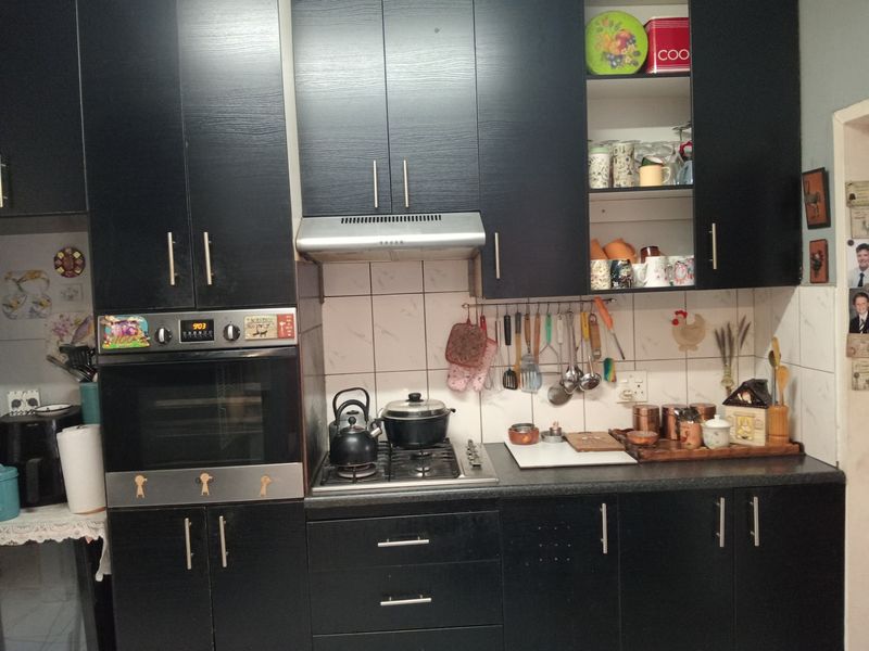 A functional kitchen featuring dark laminate cabinetry, a built-in oven, gas hob, extractor fan, and a tiled backsplash.