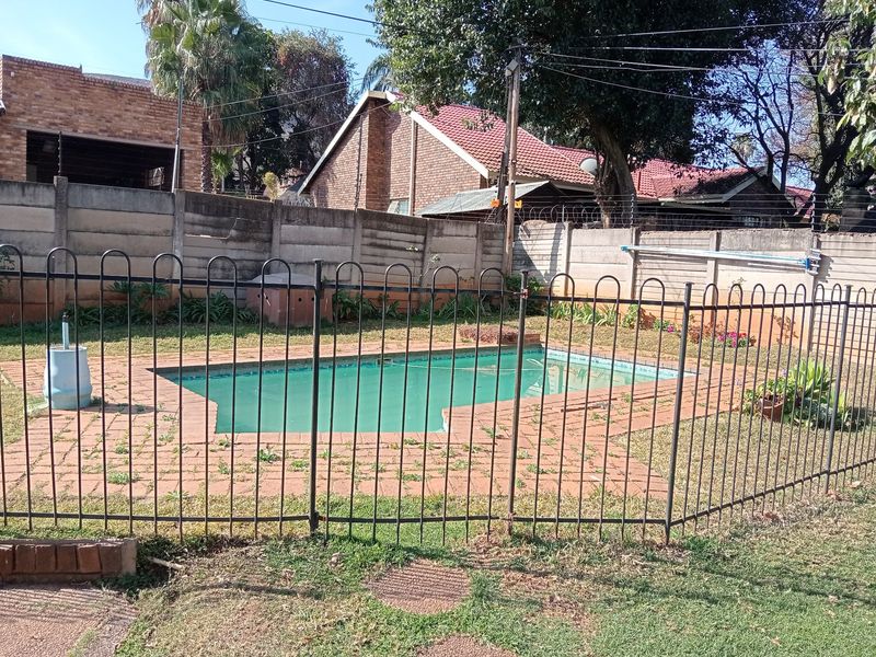 Outdoor pool area featuring a fenced swimming pool, brick paved surround, and perimeter precast concrete walling with electric fencing.