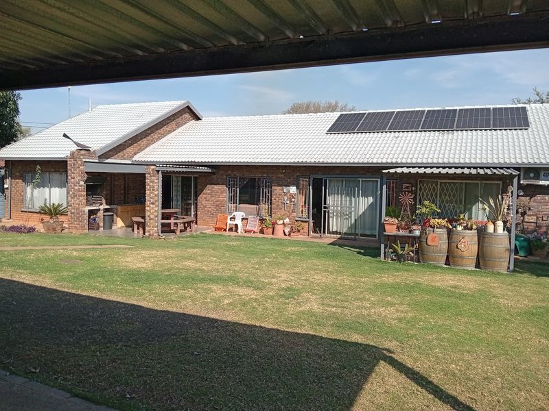 Rear view of a brick house featuring a covered patio with a built-in braai, solar panels on the roof, and a spacious garden.