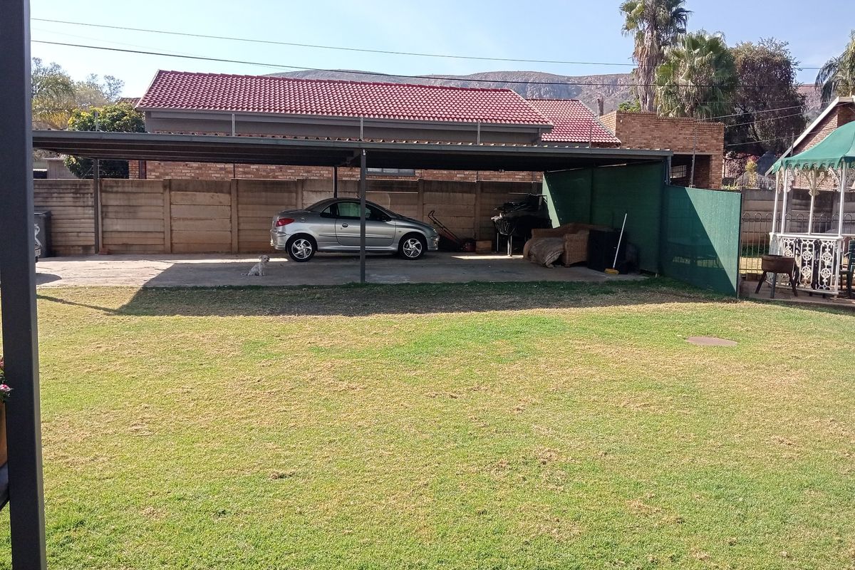 A spacious rear garden featuring a large covered carport area with concrete flooring and perimeter boundary walling.